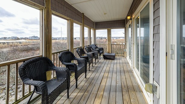 Eine überdachte Veranda mit Korbstühlen und einem Tisch, großen Fenstern und Blick auf die Landschaft.