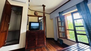 Una habitación con piso de madera, un televisor sobre un mueble, una ventana con cortinas y un equipo de aire acondicionado en la pared.