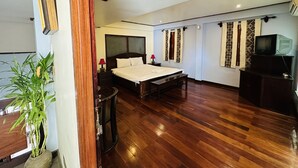 Un dormitorio amplio con una cama grande, suelo de madera, una planta en maceta, un televisor y cortinas estampadas.