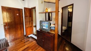 Un pasillo con piso de madera, un televisor sobre un mueble bajo y un espejo en la pared.