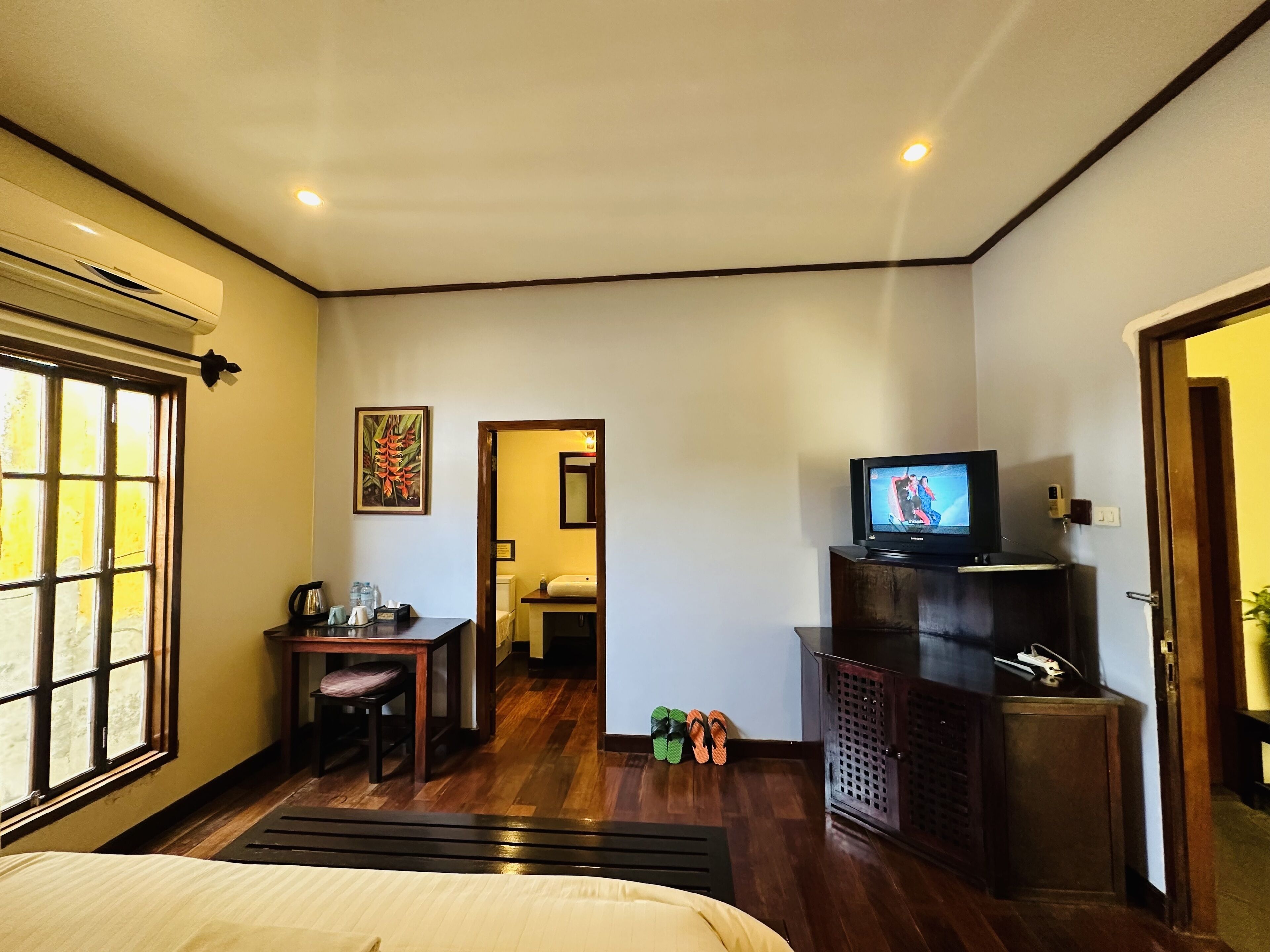 A hotel room with a bed, a desk with a chair, a television, and a bathroom visible through an open door.