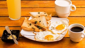 Ein Holztisch mit Frühstücksgedecke, darunter Toast, ein Spiegelei, ein Glas Orangensaft, eine Tasse Kaffee und eine kleine Schale mit Butter.