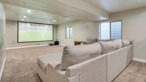 Ein Heimkinozimmer mit einer großen Leinwand, einem Ecksofa und einem Teppichboden.