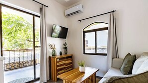Een moderne woonkamer met een bank, een houten salontafel, een aan de muur bevestigde televisie en een balkon met uitzicht op groen.