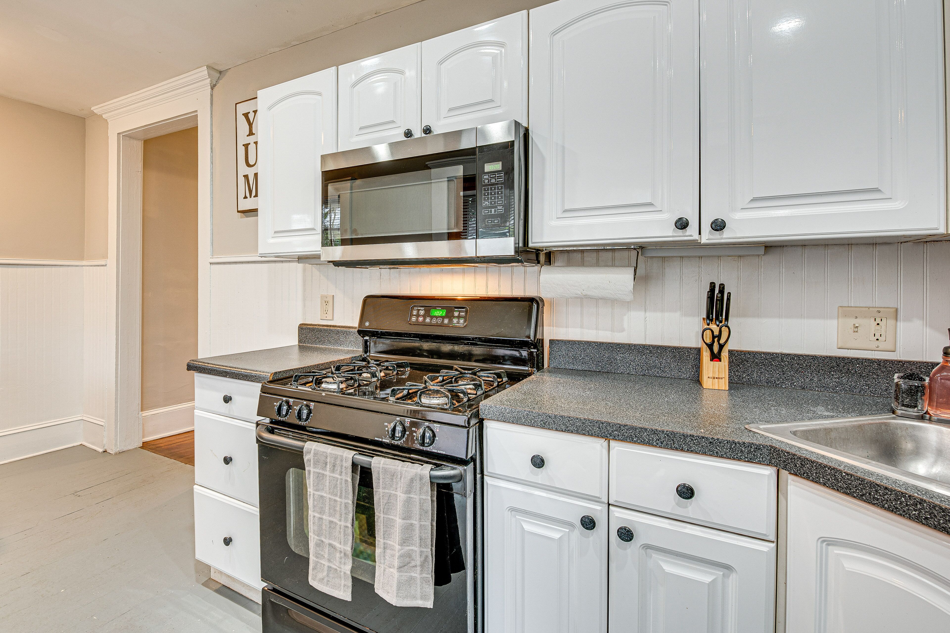A kitchen with white cabinets, a stainless steel microwave, a gas stove, and a sink.