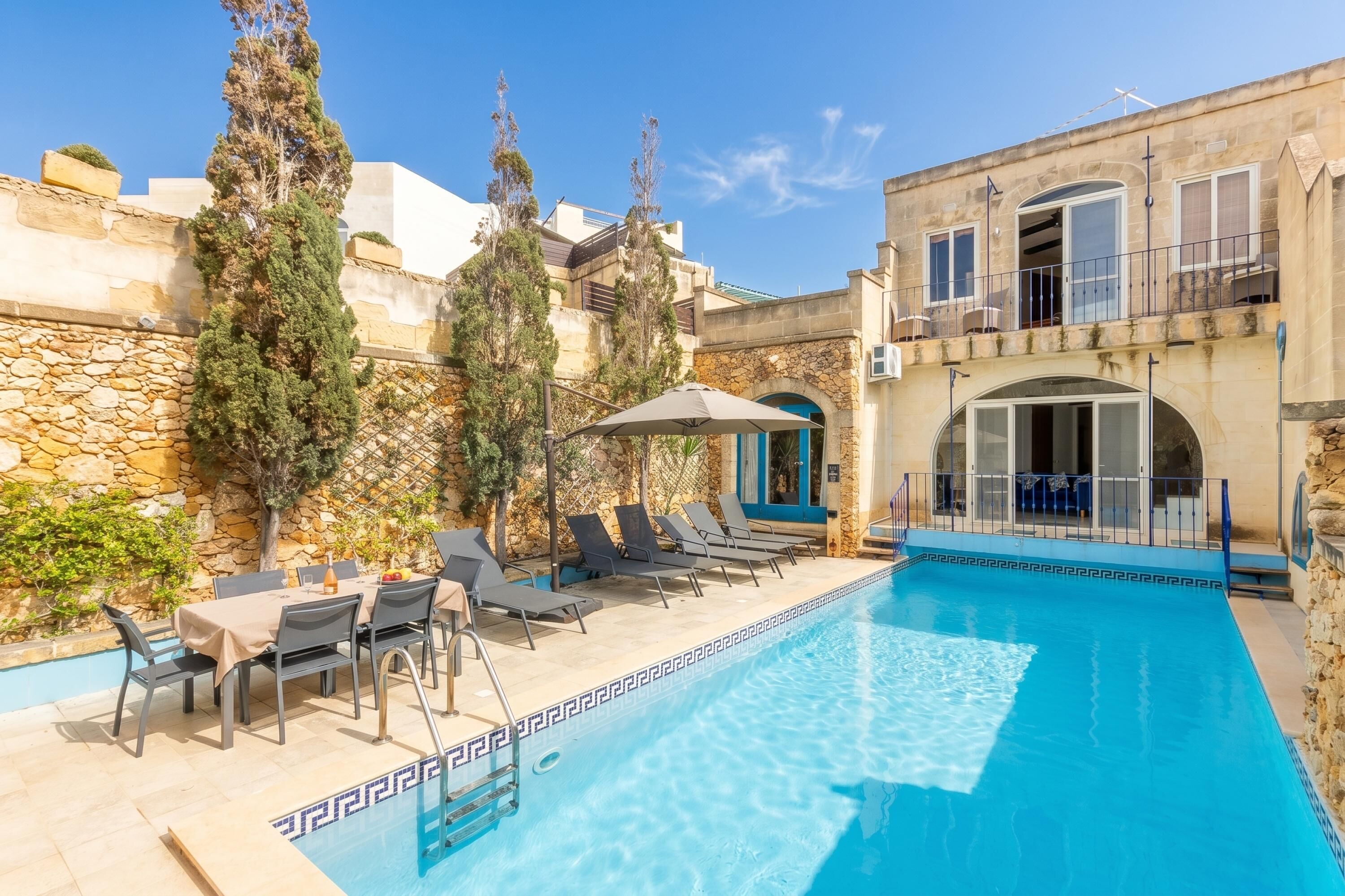 A swimming pool with lounge chairs and a table, surrounded by stone walls and trees.