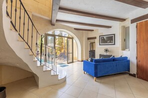 A spacious living area with a blue sofa, a staircase with a glass railing, and a wooden door. - Dionisia Gozitan Villa and Pool (Ghasri)