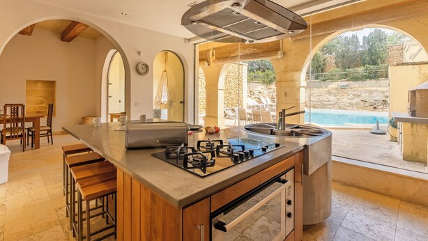 A modern kitchen with an island, built-in oven, and a view of an outdoor swimming pool. - Onefifty Gozitan Villa and Pool (Xaghra)