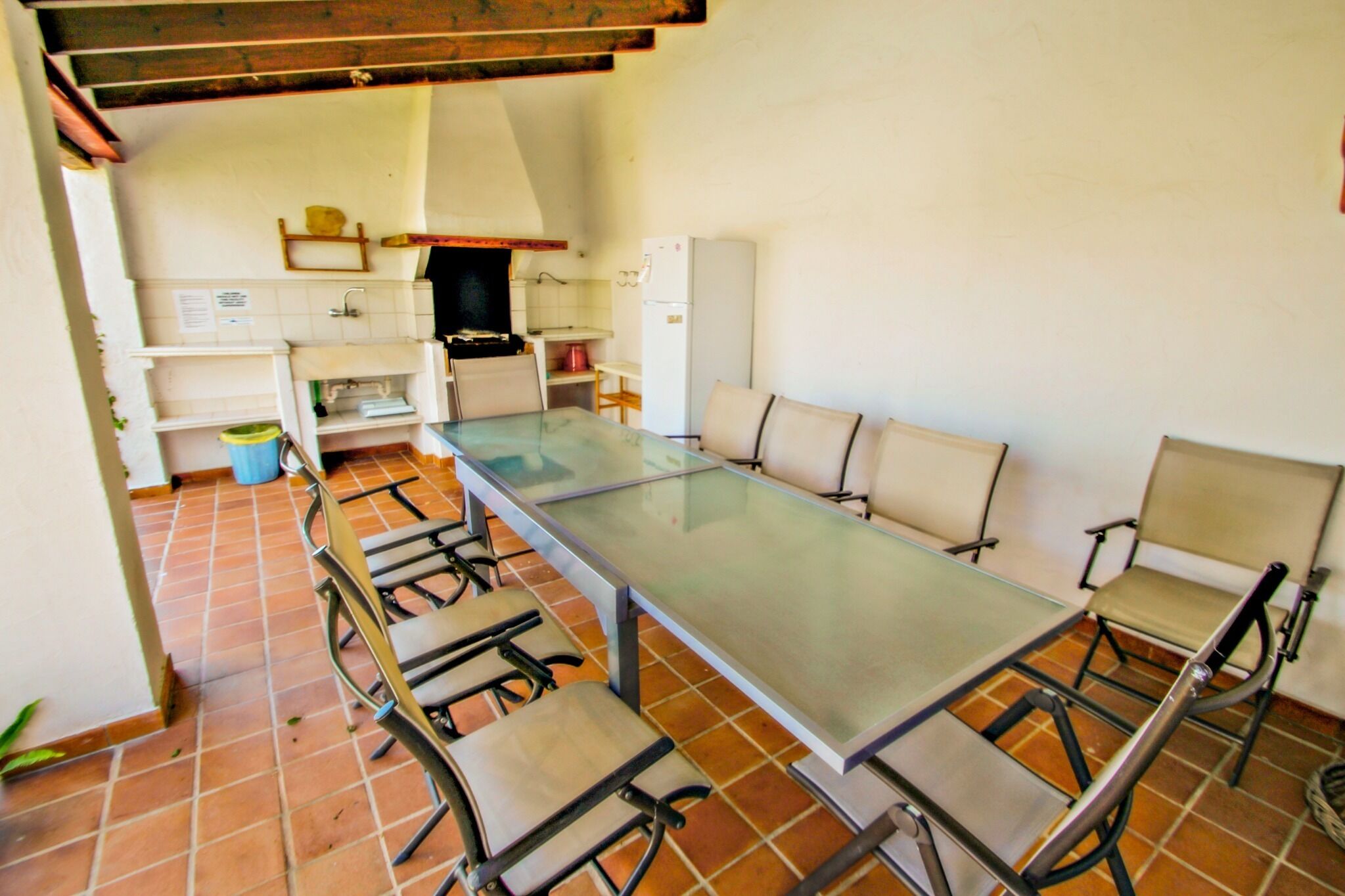 Una zona de dinar amb una taula llarga i sis caires, una cuina al fons i un paviment de rajoles.