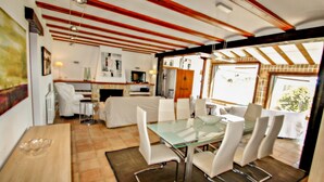 A dining area with a glass table and white chairs, a kitchen in the background, and wooden beams on the ceiling. - Finca La Coma - modern, well-equipped villa with private pool in Benissa (Benissa)