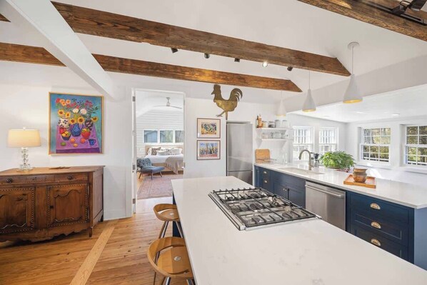 A modern kitchen with a central island, wooden beams, and a rustic rooster decoration.