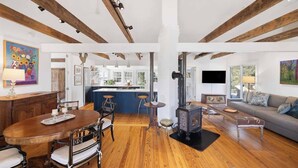 A spacious living area with a wooden floor, a fireplace, a dining table with chairs, a sofa, and a kitchen in the background. - Entire Cottage on Equestrian Farm with Zebras (Charlottesville)
