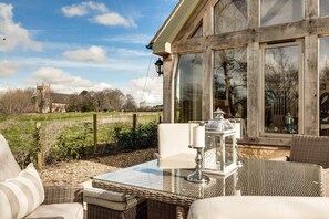 A glass-enclosed patio with wicker furniture, a table, and a lantern. - Hiron's Piece and Honeysuckle Cottage with Hot Tub (Weston Subedge)