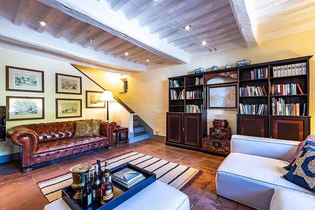 A cozy living room with a leather sofa, a white armchair, a bookshelf, and a staircase.