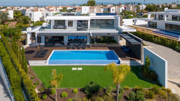 Ein modernes, mehrgeschossiges Wohngebäude mit Pool auf dem Dach, umgeben von üppiger Vegetation und freiem Blick auf das Meer.