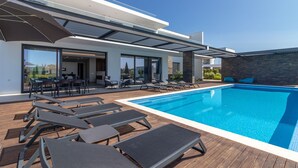 Ein moderner Poolbereich im Freien mit Liegestühlen und Essbereich.