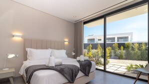 Ein modernes Schlafzimmer mit einem großen Bett, Nachttischlampen und Blick auf ein Gebäude und Bäume durch raumhohe Fenster.
