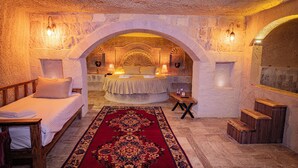 A room with a bed, a wooden bench, a red patterned rug, and stone walls. - Sur Cave Hotel (Ürgüp)
