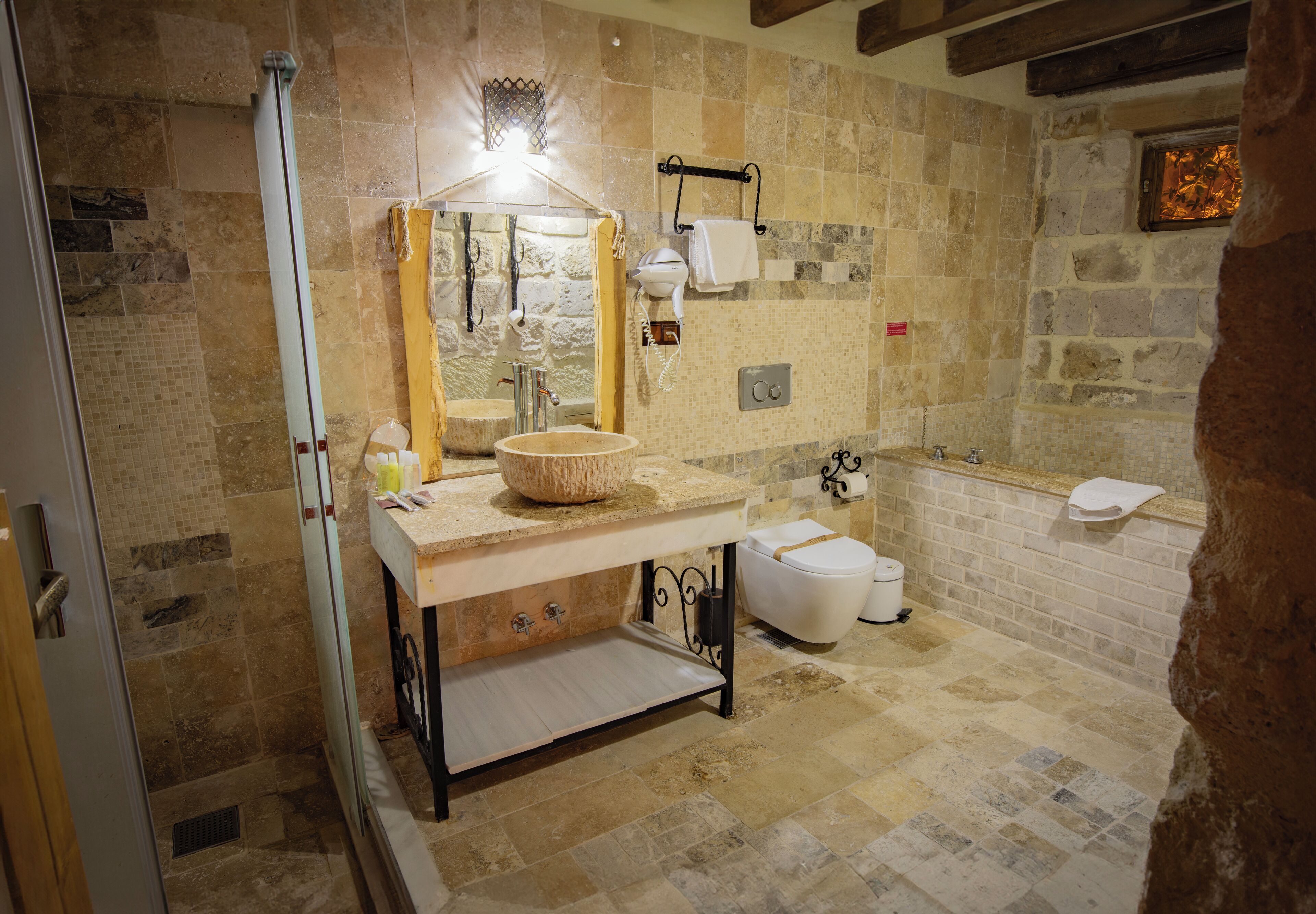 A bathroom with a stone-tiled floor, a sink with a stone basin, a mirror, a towel rack, and a toilet.