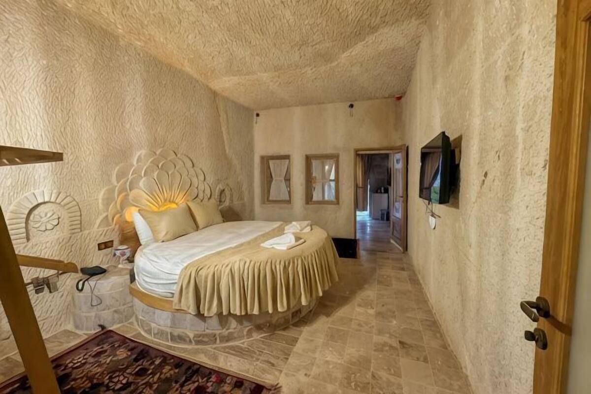 Une chambre à coucher avec un lit rond, une porte en bois, un téléviseur fixé au mur et un couloir menant à une autre pièce.