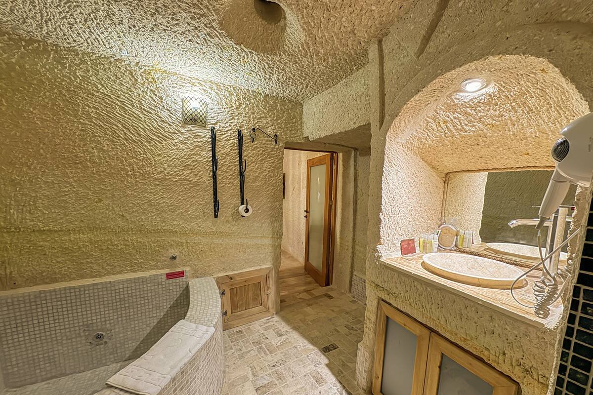 Une salle de bain avec un mur en pierre, une baignoire, une porte en bois et un lavabo avec un miroir.