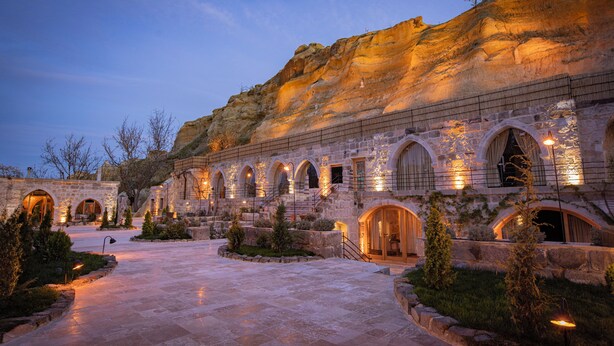 A historic building with arched windows and stone walls, featuring a courtyard with stone pathways and small trees. - Sur Cave Hotel (Ürgüp)
