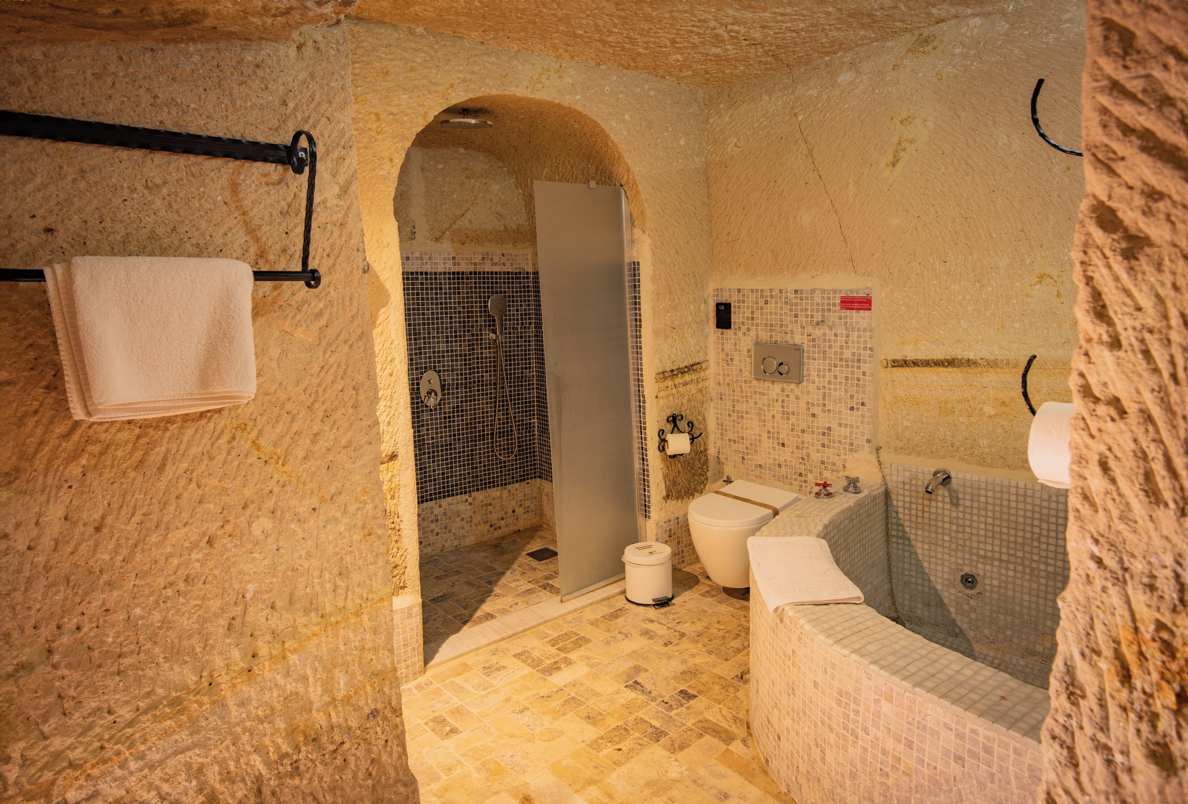 A bathroom with a mosaic floor, a bathtub, a toilet, and a shower area.