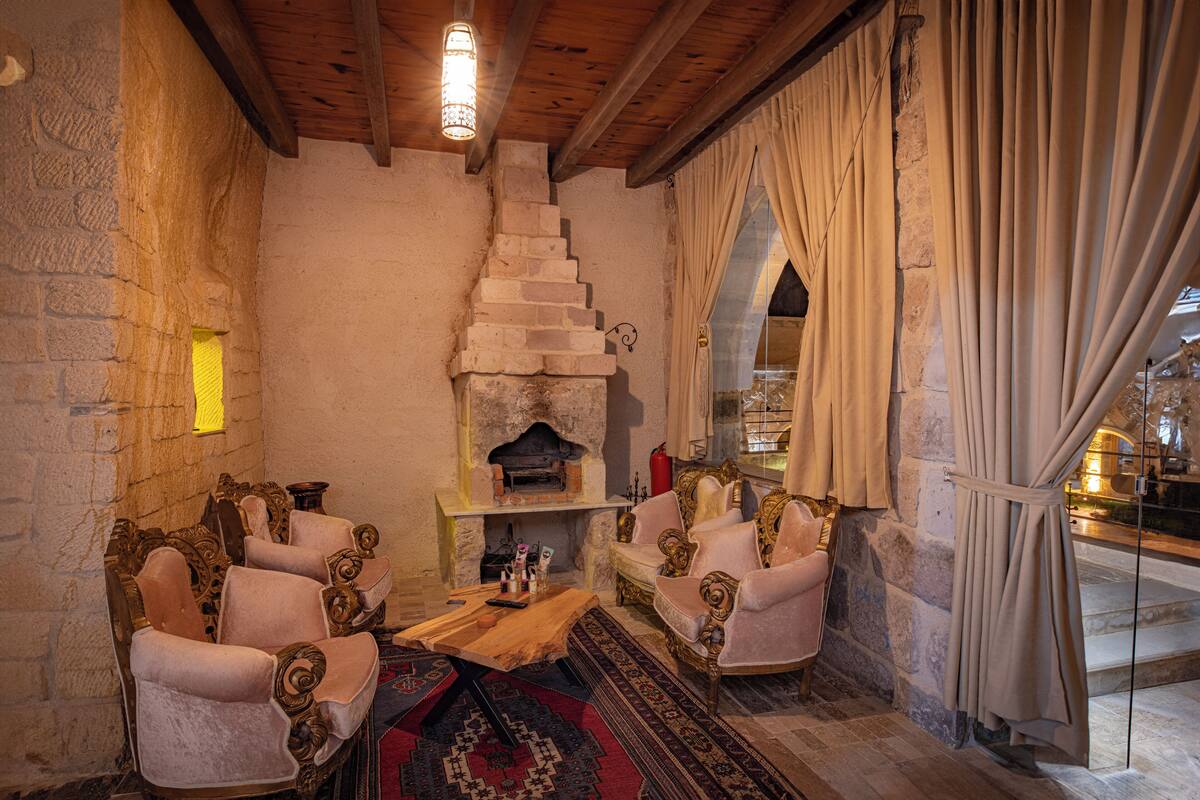 Une pièce chaleureuse avec une cheminée, deux fauteuils décoratifs, une table en bois et un tapis à motifs.