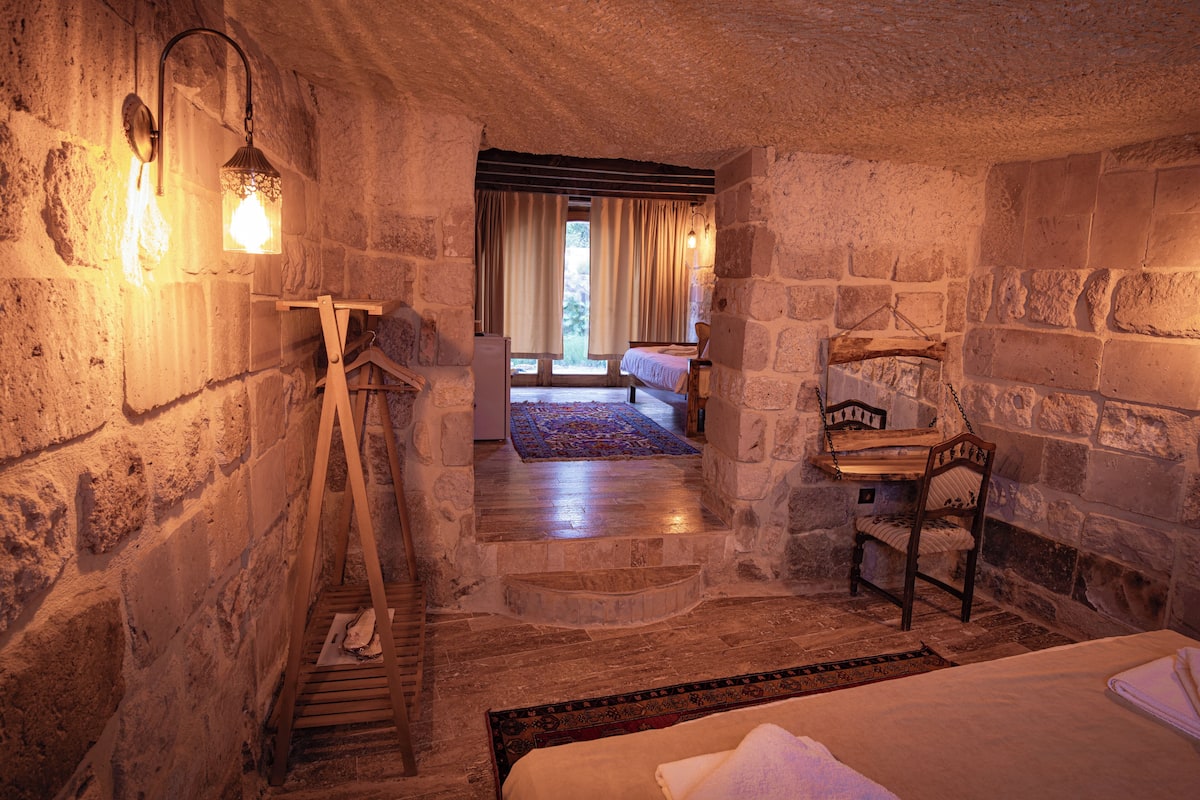 Une chambre aux murs de pierre, avec une échelle en bois, un lit, une chaise et une étagère en bois.