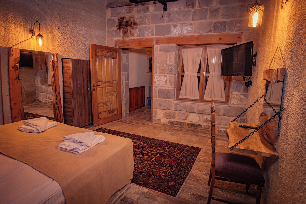 Une pièce chaleureuse avec un lit, une chaise en bois, un mur en pierre et un luminaire suspendu.