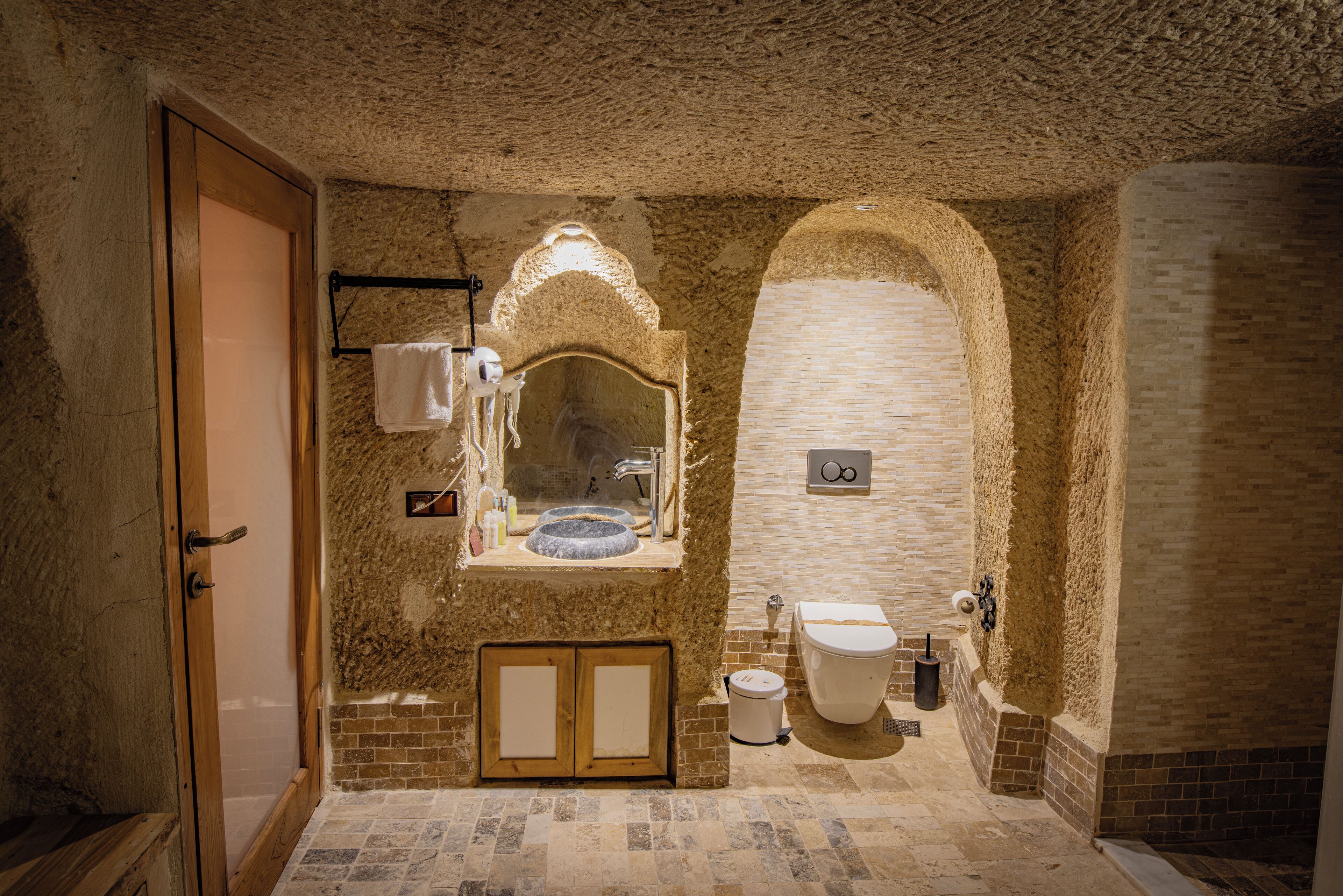A bathroom with a stone wall, a wooden door, a sink, and a toilet.