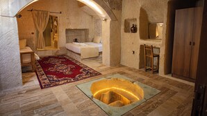 A room with a stone archway, a bed, a wooden cabinet, and a unique circular light feature on the floor. - Sur Cave Hotel (Ürgüp)