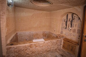 A stone-walled bathroom with a bathtub, a wooden cabinet, and a shower area. - Sur Cave Hotel (Ürgüp)