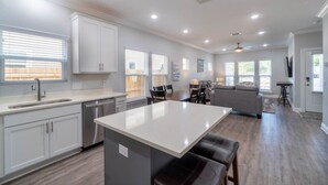 Une cuisine moderne avec un îlot central, un coin repas avec des chaises et un salon avec un canapé.