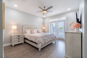A bedroom with a bed, nightstands, a ceiling fan, and a view through a door.