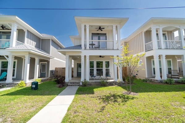 A residential building with a central entrance, two balconies, and a small front yard with a tree.