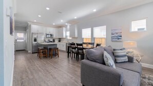 A modern kitchen with white cabinets, a dining area with a gray sofa, and a small table with chairs.