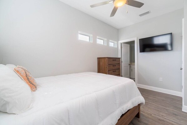 A bedroom with a bed, a ceiling fan, a TV mounted on the wall, and a wooden dresser. - Urban Vista & Flat - Family Friendly (Pensacola)