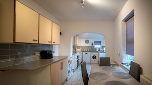 Une cuisine compacte avec un coin repas, comprenant des placards, un plan de travail, un évier, un lave-linge et une table à manger avec des sets de table.