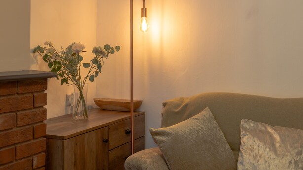 Une pièce chaleureuse avec une cheminée en briques, une petite table en bois sur laquelle est posé un vase de fleurs, et une lampe sur pied au design moderne.