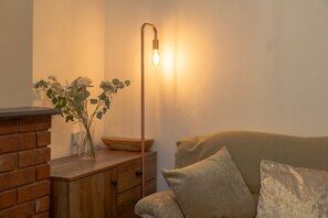 Une pièce chaleureuse avec une cheminée en briques, une petite table en bois sur laquelle est posé un vase de fleurs, et une lampe sur pied au design moderne.