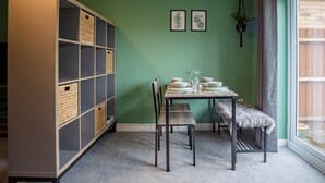 Een eethoek met een tafel voor vier personen, een bank en een boekenkast met manden.