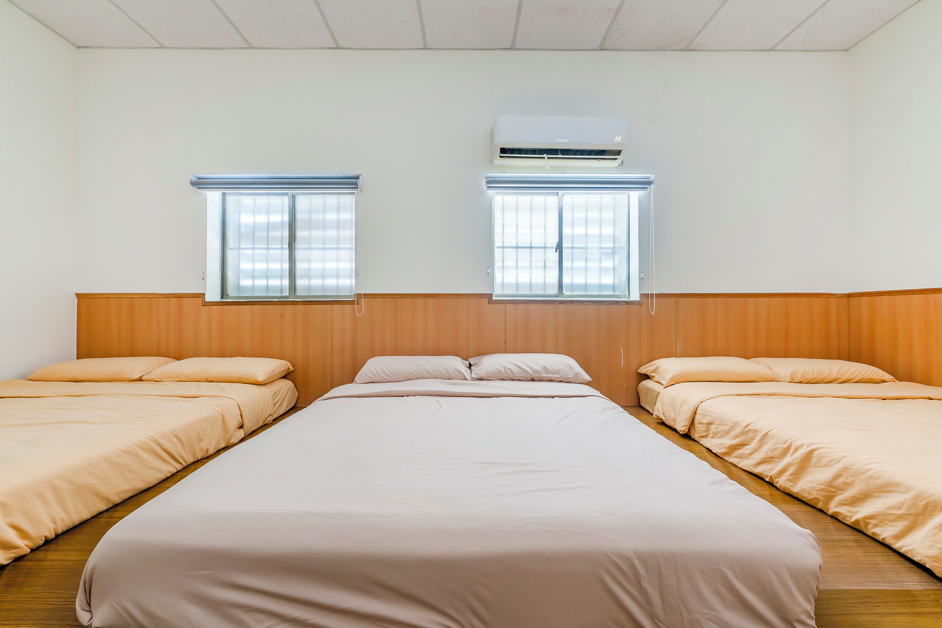 Une chambre avec deux lits, une tête de lit en bois et deux fenêtres équipées de stores.