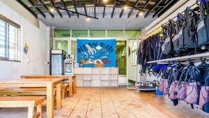 Interior de restaurante con mesas y bancos de madera, un estandarte azul con ilustraciones de vida marina, y equipo de buceo a la vista.