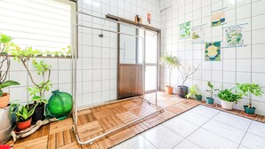 Una habitación con piso de madera, paredes de baldosas y varias plantas en macetas.