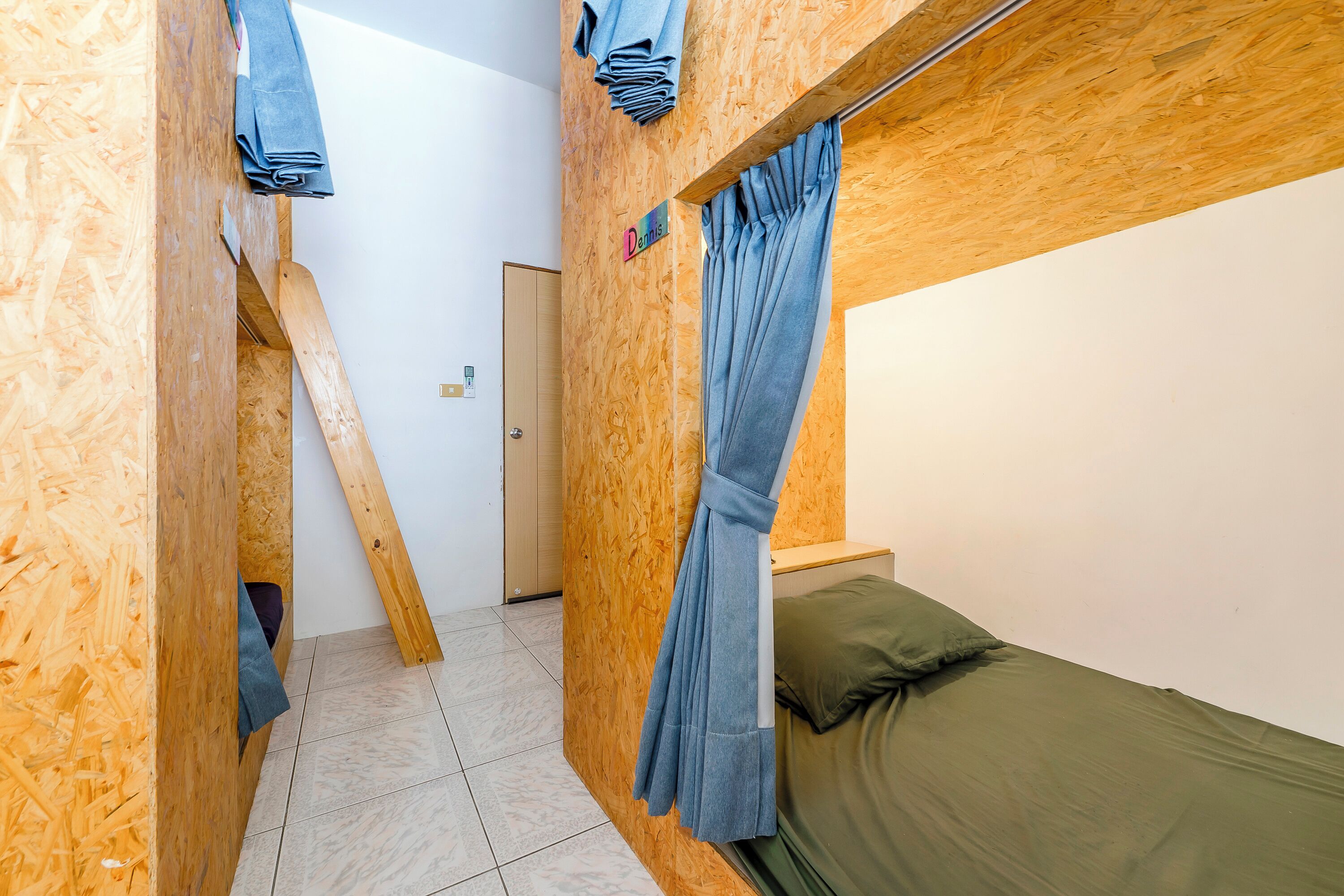 A room with a bunk bed, wooden walls, a door, and a curtain.
