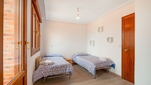 Una habitación con dos camas, suelo de madera, pared de ladrillo y una puerta.
