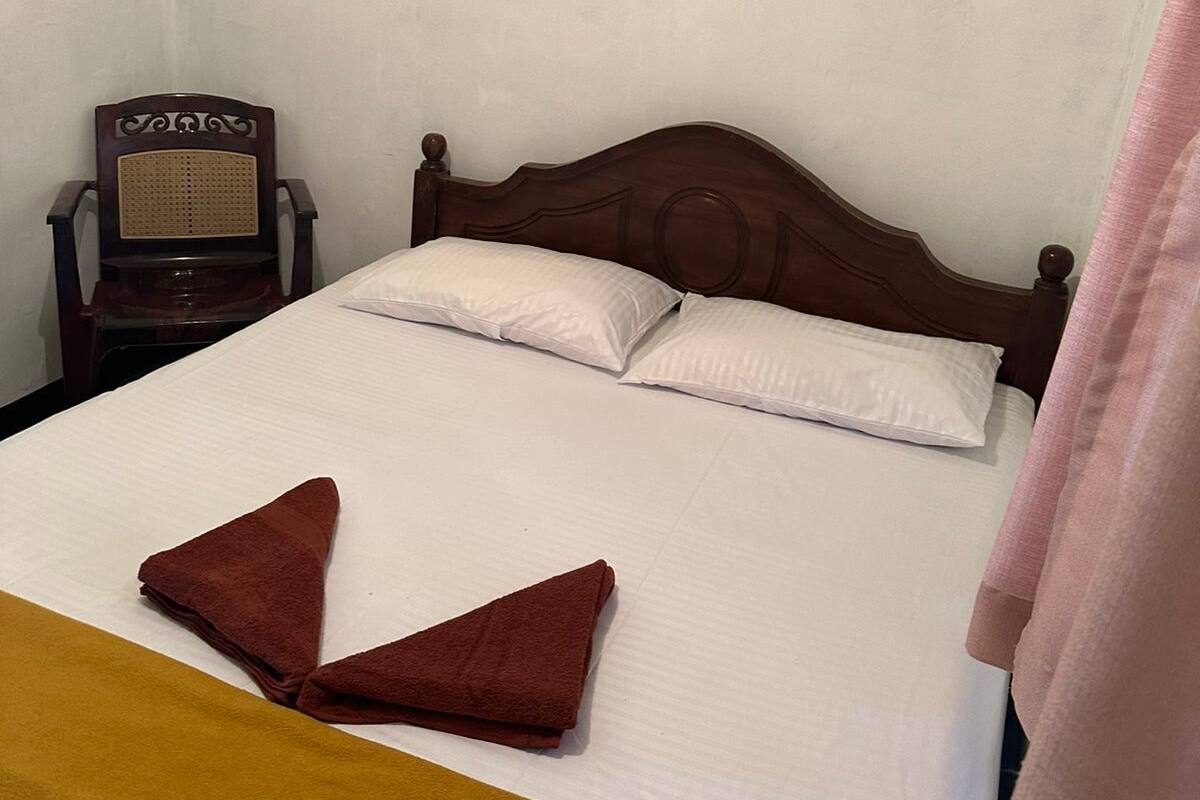 A single bed with a wooden headboard, two white pillows, and a brown towel folded on the bed.