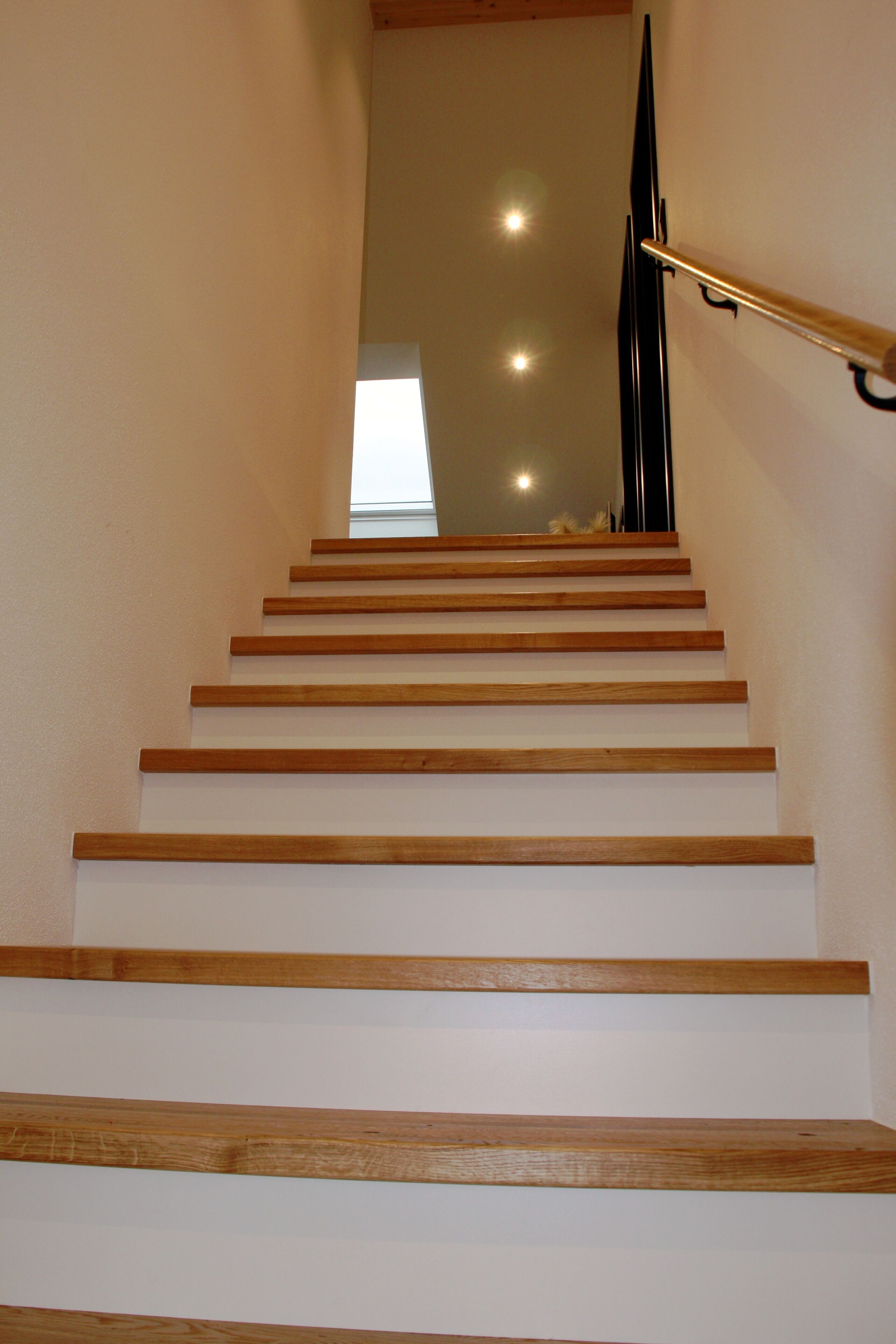 Eine Holztreppe mit Handlauf, die zu einem Zwischenpodest mit einem Fenster führt.