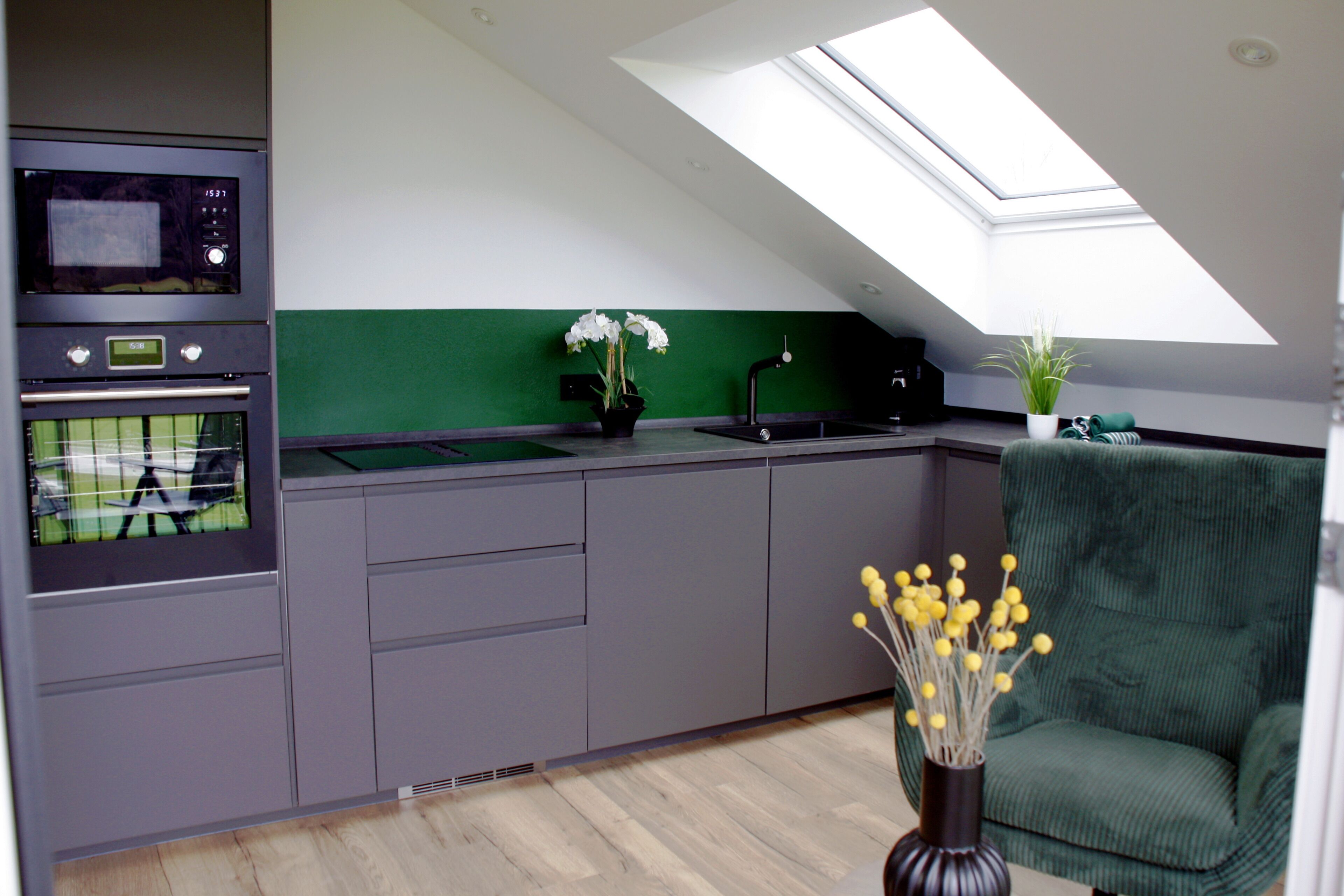 Una cocina moderna con tragaluz, horno empotrado y una pared verde decorativa.